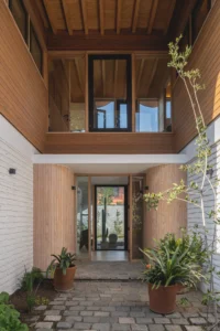 Entrance passage between brick walls with a timber clad bridge above and potted plants on cobbles, Los Navegantes House