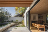 Sliding glass wall opening a living room with leather armchairs onto a courtyard with a curved bench, Los Navegantes House