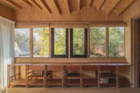 Long timber desk with four chairs below a band of windows in a wood lined room, Los Navegantes House