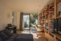 Ground floor family room with a sofa, piano and wall of wooden shelving opening to the garden, Los Navegantes House
