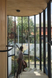 Figure descending the helical stair inside the glazed cylinder with trees outside, Los Navegantes House