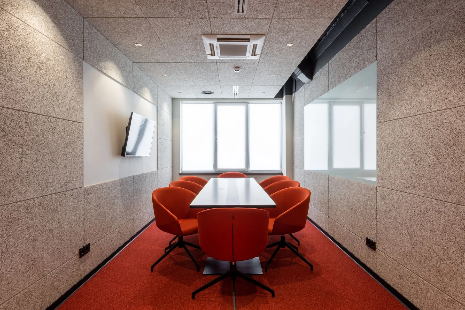 Meeting room lined with fabric acoustic wall panels around a table and red chairs