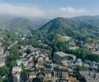 Aerial view of the village rooftops in a green mountain valley with the theater among them, Moganshan Liaoyuan Theater by One Design