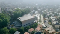 Hazy aerial view of the theater's angular roof beside a tree lined village street, Moganshan Liaoyuan Theater by One Design