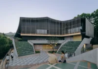 Front plaza with green stepped seating in two amphitheaters below the louvred facade, Moganshan Liaoyuan Theater by One Design