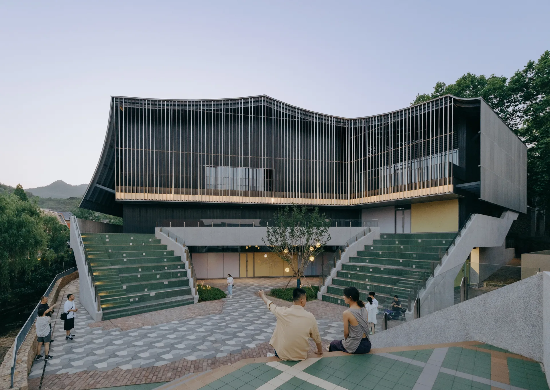Front plaza with green stepped seating in two amphitheaters below the louvred facade, Moganshan Liaoyuan Theater by One Design