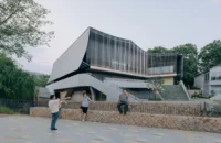 People sitting on a stone wall in the square in front of the theater's tilted concrete base, Moganshan Liaoyuan Theater by One Design
