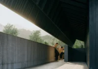 Visitors leaning on a concrete wall below the dark angled roof overhang, Moganshan Liaoyuan Theater by One Design