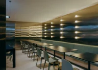 Café interior with long tables and chairs before a wall of rippled metal and small lights, Moganshan Liaoyuan Theater by One Design