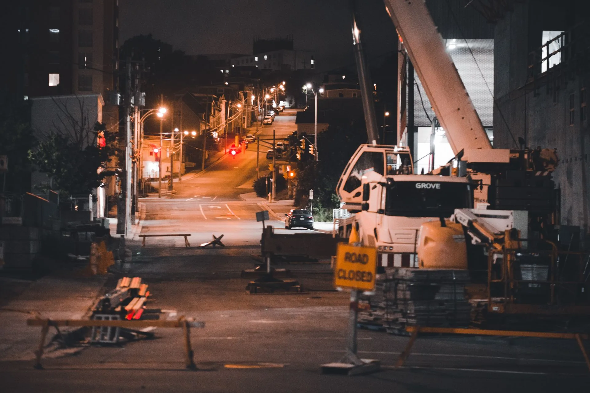City street closed at night with a mobile crane, barriers and a road closed sign