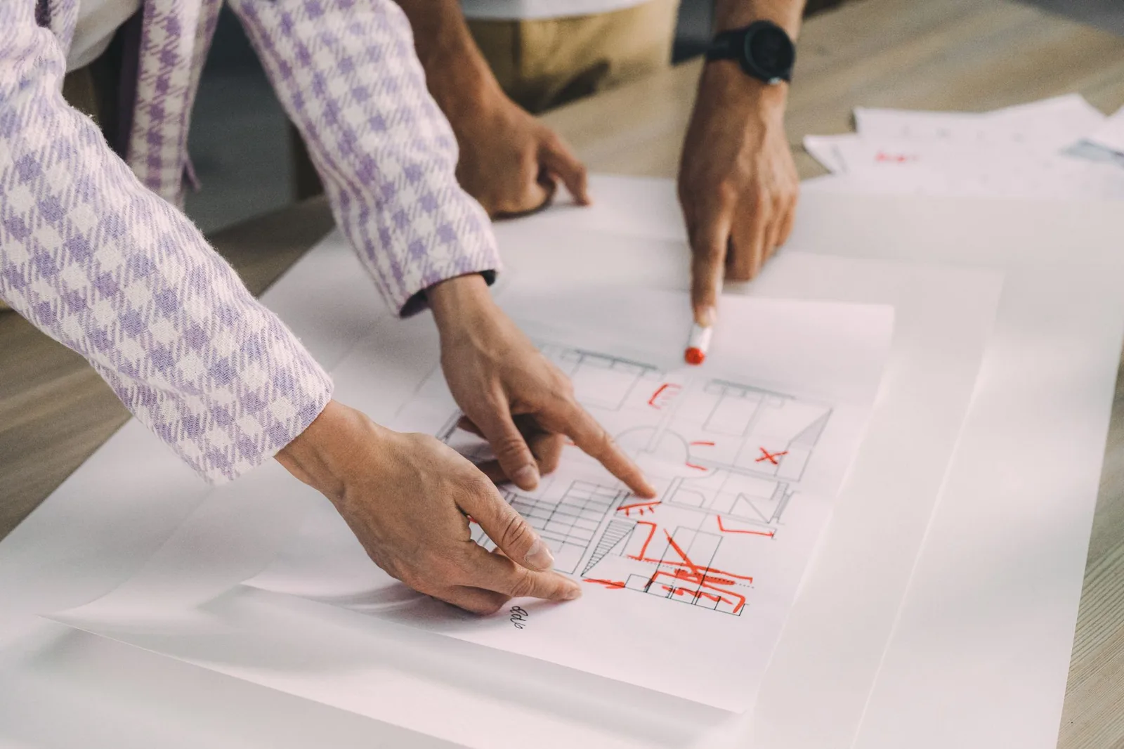 Hands marking corrections on printed architectural drawings during a design review