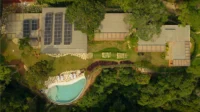 Aerial view of the flat roofs, solar panels, gardens and kidney shaped pool among trees, Pedra Azul House by Escala Arquitetura