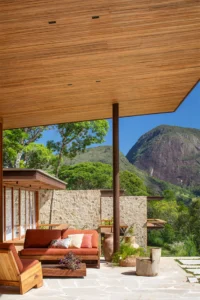 Terrace with orange cushions beneath a deep wooden soffit on a slender column, Pedra Azul House by Escala Arquitetura