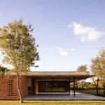 Low brick and concrete house under a thin flat roof with a perforated brick screen and an open gallery in a grassy clearing