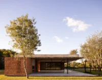 Low brick and concrete house under a thin flat roof with a perforated brick screen and an open gallery in a grassy clearing