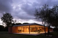 Corner of the house at twilight with warm light inside the open gallery and storm clouds above