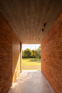 Narrow brick passage with a concrete ceiling framing a view to the lawn