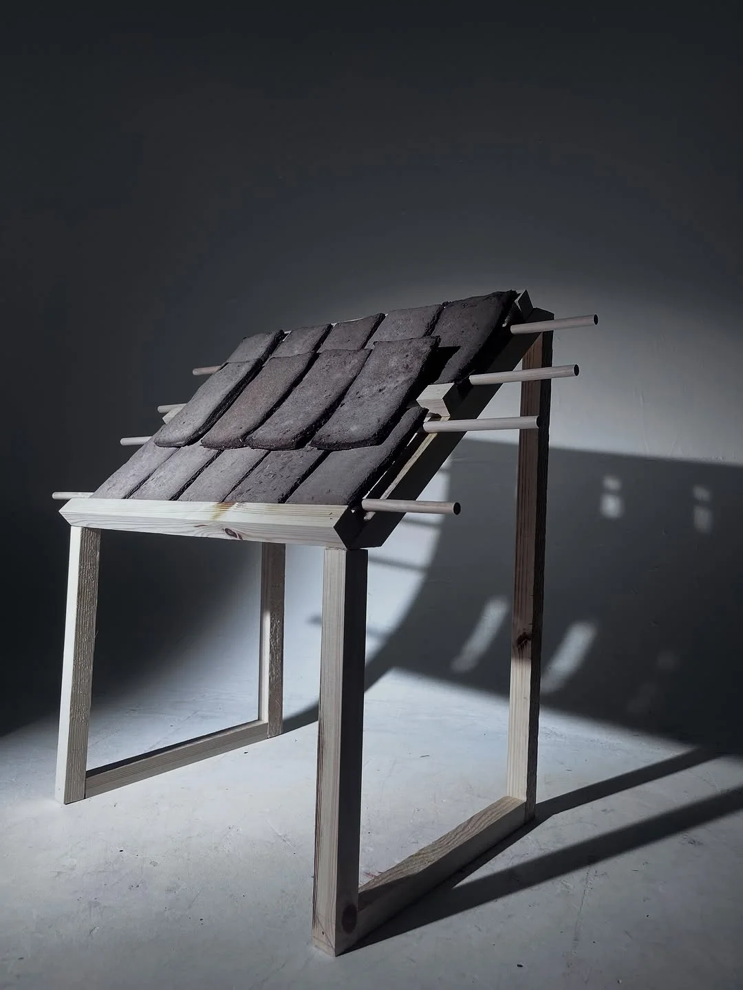 Dark wood slat frame model lit from the side so long shadows define its structure