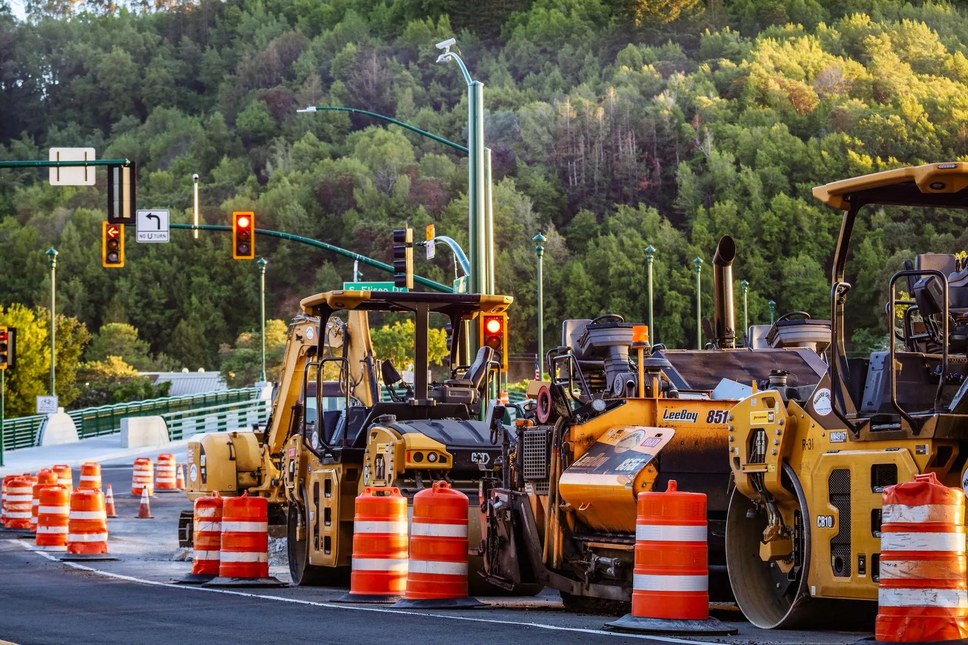 Road rollers, paving machines and orange traffic barrels at a roadworks site beside traffic lights