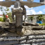 Close-up of a 3D concrete printer nozzle laying a fresh bead of concrete on top of a layered printed wall