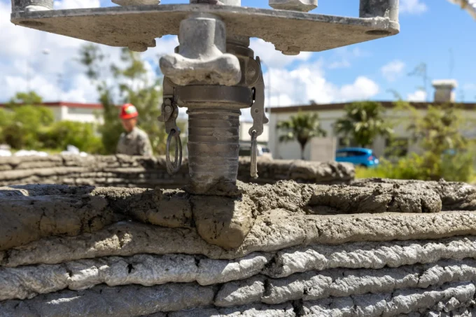 Close-up of a 3D concrete printer nozzle laying a fresh bead of concrete on top of a layered printed wall