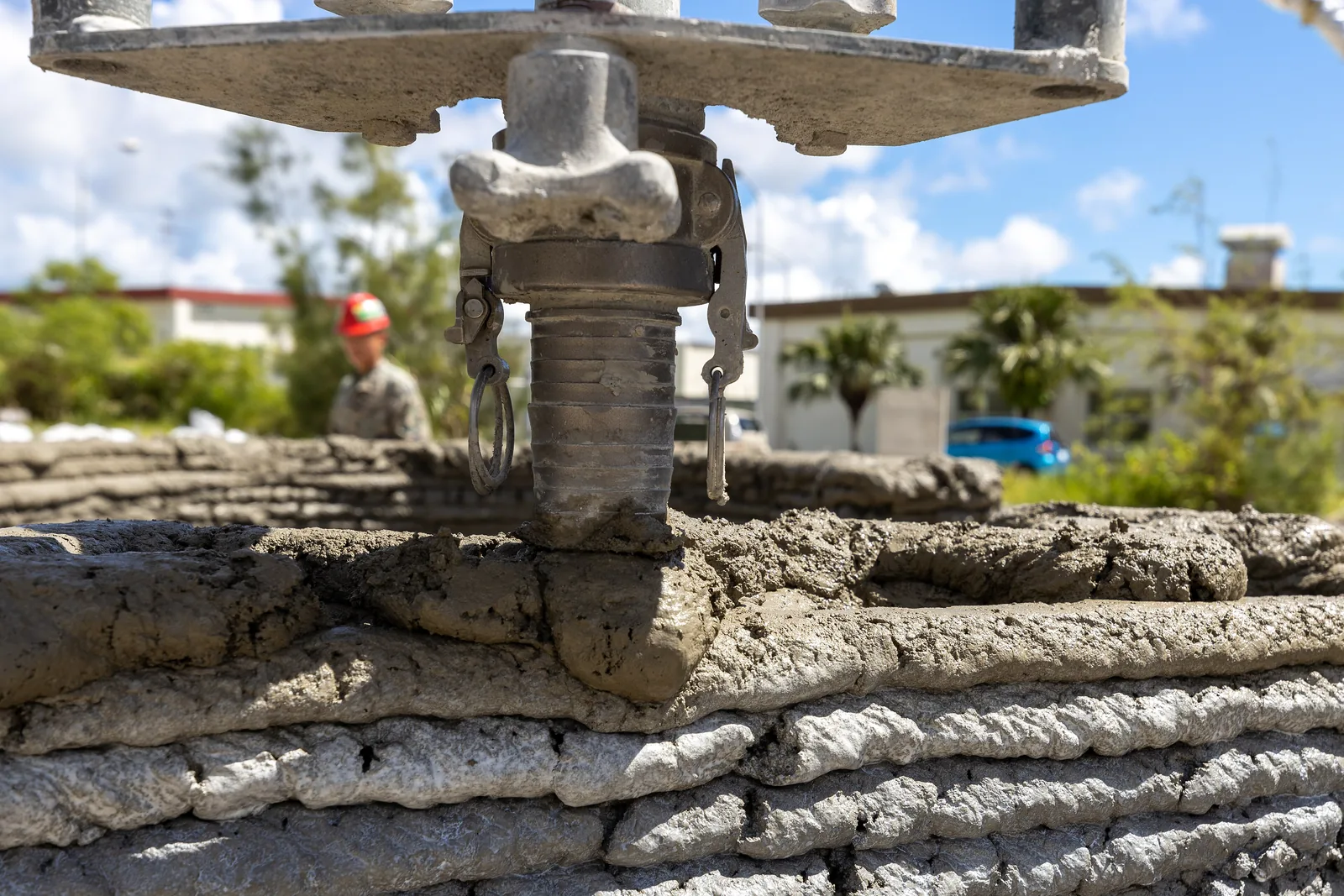 Close-up of a 3D concrete printer nozzle laying a fresh bead of concrete on top of a layered printed wall