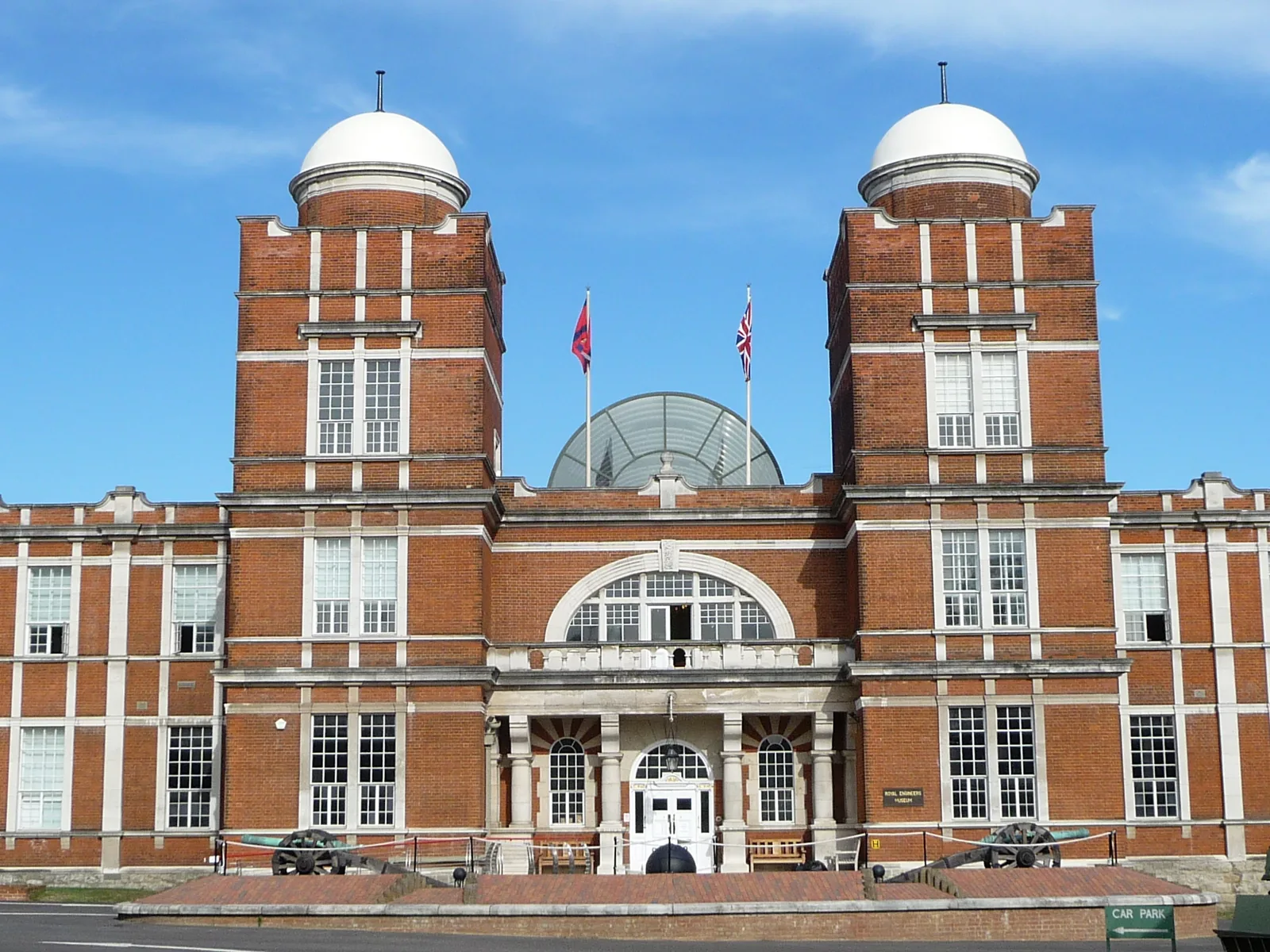 Red brick facade of the Royal Engineers Museum with two domed towers, flags and a central glazed entrance