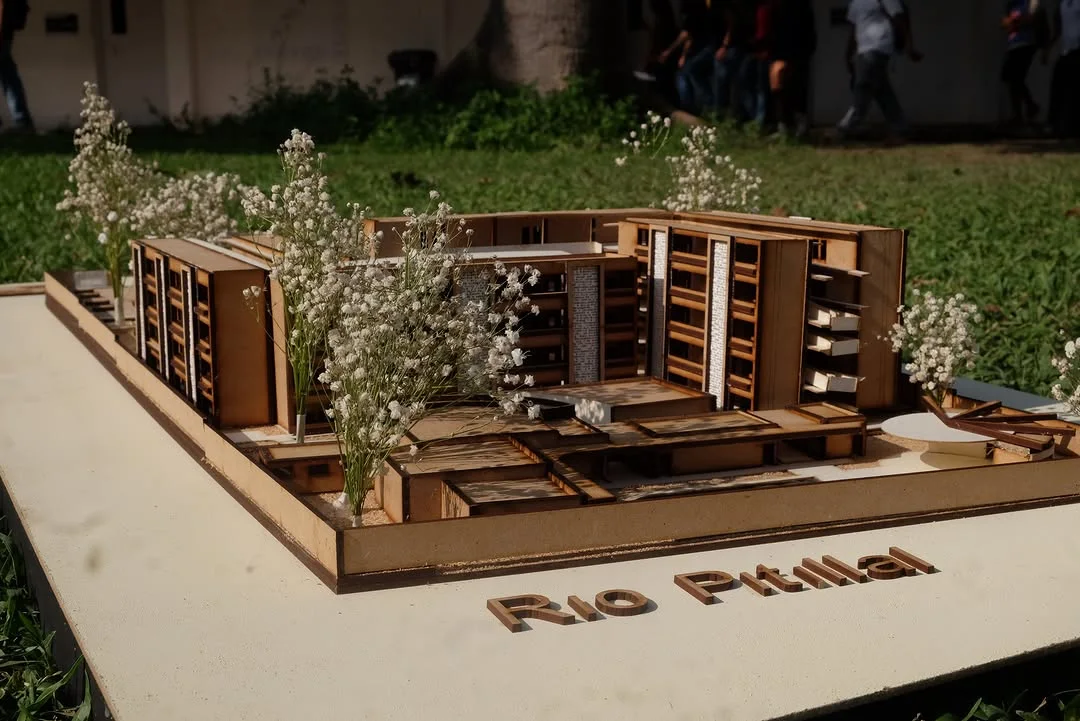 Wooden competition site model with planted courtyards displayed outdoors on a labeled base