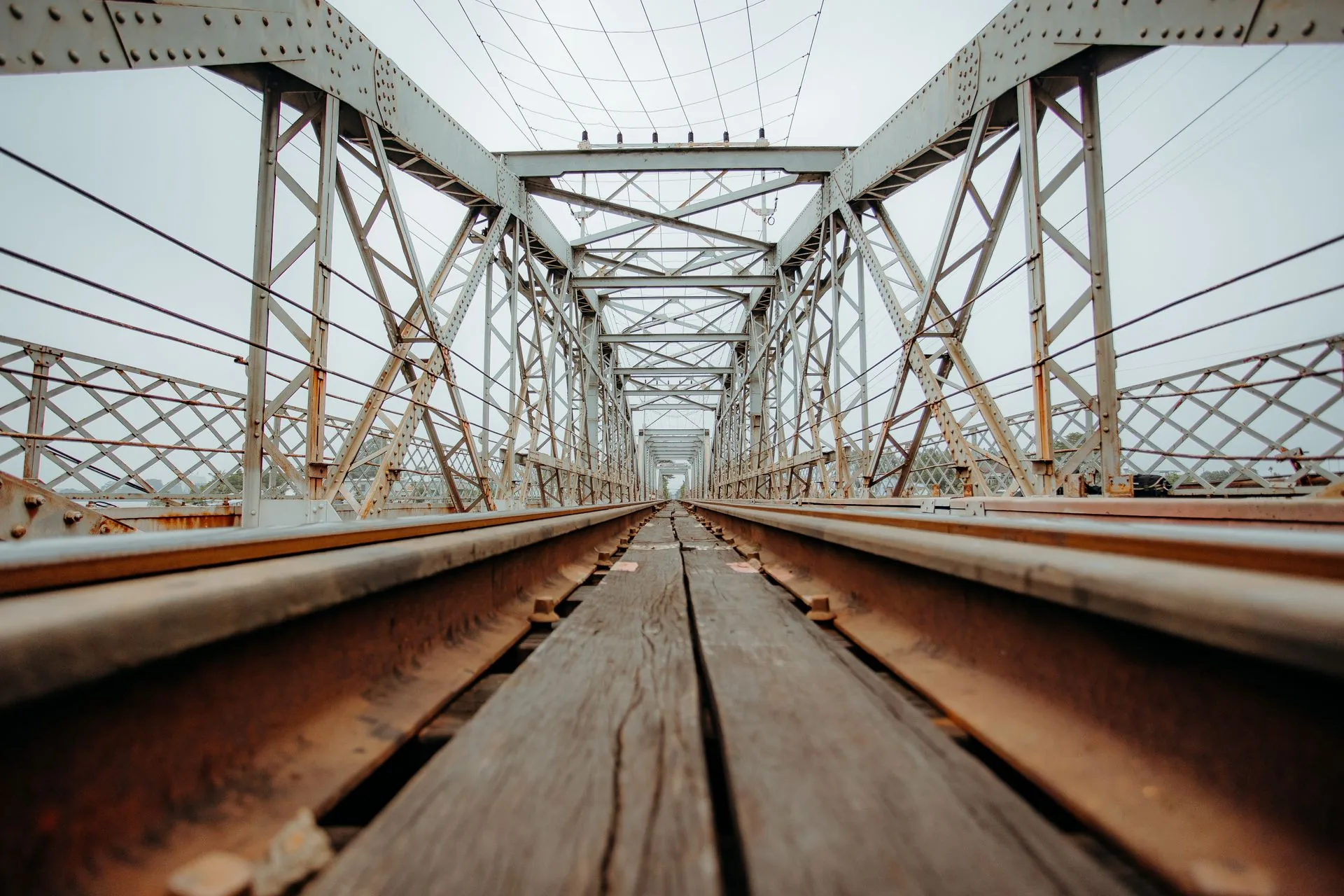 Perspective along an old steel truss railway bridge with a timber walkway between the rails