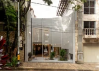 Building front with a curved metal mesh screen between older neighbours and a timber pavement