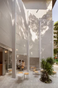 Tall perforated screen rising above people sitting at café tables beside a palm
