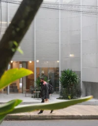 Pedestrian walking past the metal screen and forecourt seen through tree branches