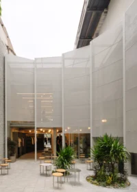 Curved mesh facade wrapping the upper floors above the planted forecourt
