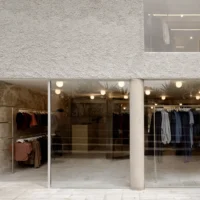 Glazed shop front with clothing rails behind a round concrete column and rough walls