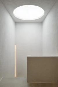 Round skylight above a white room with a stone counter and a vertical light slot