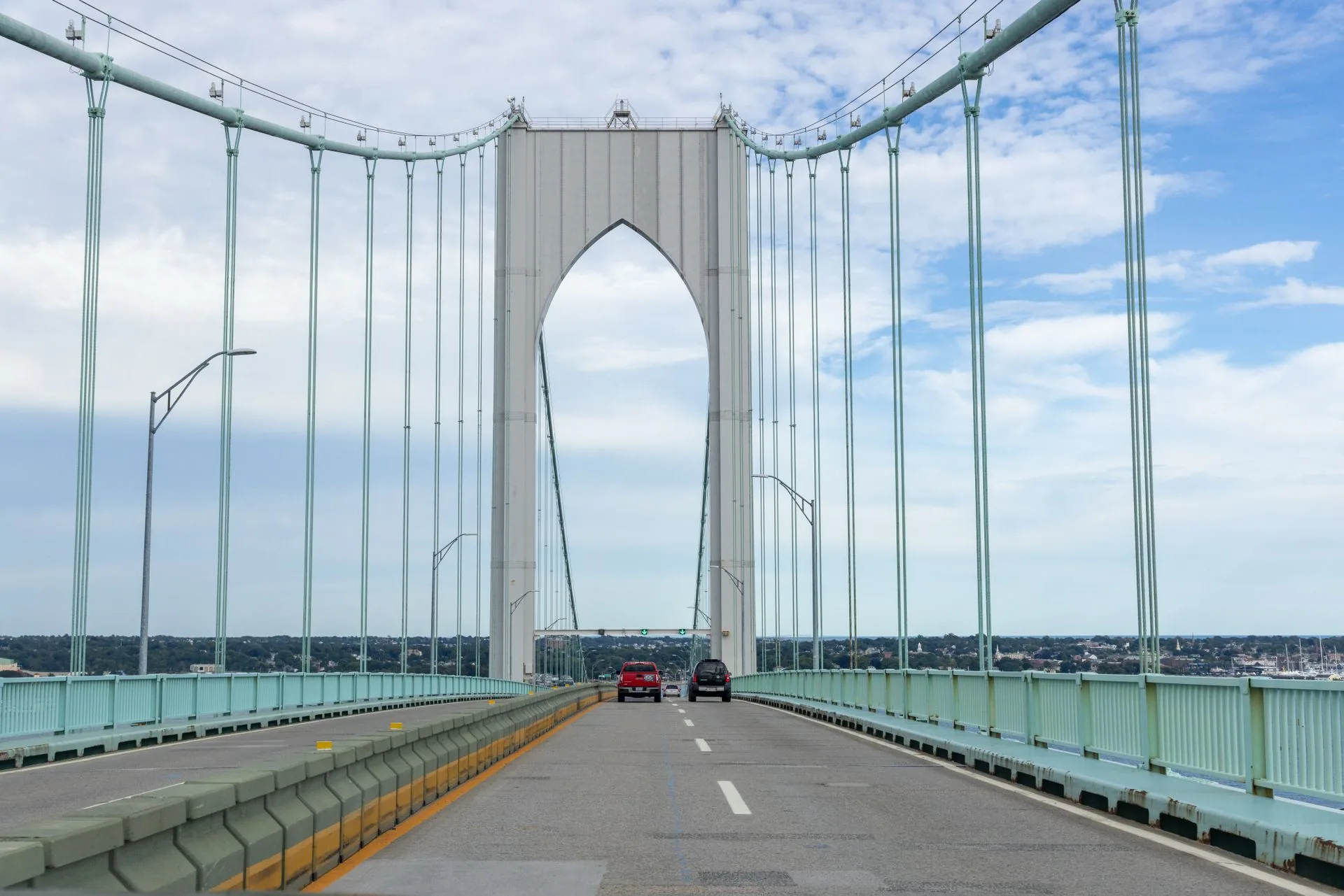 Traffic lanes crossing a suspension bridge deck toward a pointed arch tower