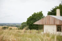 Gable end with larch boarded roof and plastered wall facing open farmland, The Makers Barn by HUTCH design