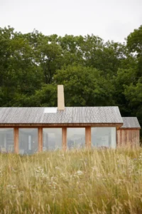 Long elevation of glass panels between timber posts behind tall summer grasses, The Makers Barn by HUTCH design