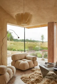 Armchair beside a curving floor lamp in front of a full height glass corner, The Makers Barn by HUTCH design