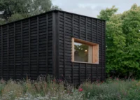 Small black charred timber cabin with a deep timber framed window set in a wildflower garden, The Yakisugi Cabin