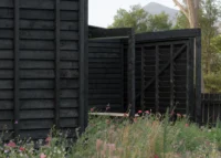 Charred board walls of the cabin and a slatted gate with a mountain peak behind, The Yakisugi Cabin