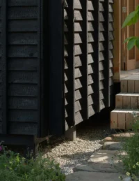 Timber steps and stone path at the corner of the raised cabin with charred cladding, The Yakisugi Cabin