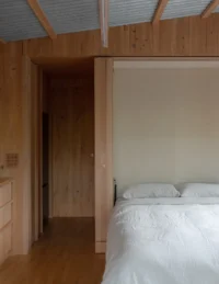 Bed set into the joinery with a doorway to the walk in robe beyond, The Yakisugi Cabin