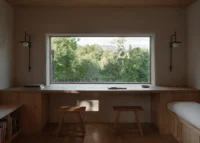 Long timber desk with two stools under a wide window framing trees, The Yakisugi Cabin