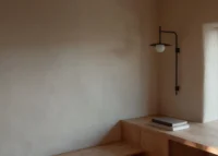 Corner of smooth clay plaster wall with a black wall lamp over a timber desk, The Yakisugi Cabin