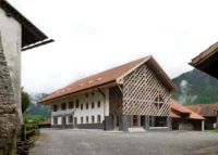 Long whitewashed farmhouse with a red tile roof and timber lattice gable at the end of a gravel yard
