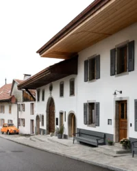 Street front of the farmhouse with white render, grey shutters, arched doorways and deep timber eaves