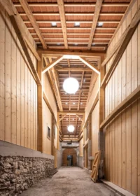Tall timber clad corridor through the former barn with a stone base wall and pendant lamps