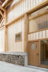 New timber wall with a porthole door set on the old rubble stone base inside the barn