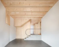 White room with a timber ceiling and a concrete stair rising behind a curved handrail